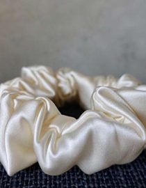White Colored Silk Scrunchie Kept On A Grey Colored Fabric